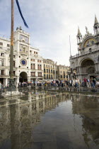 Aqua Alta High Water flooding in St Marks Square with tourists on elevated walkways above the flooded piazza beside St Marks Basilica and the Torre dellOrologio clock tower