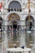 Aqua Alta High Water flooding in St Marks Square with pigeons on a dry piece of the piazza with St Marks Basilica beyond