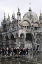 Aqua Alta High Water flooding in St Marks Square with tourists walking on elevated walkways above the water beside St Marks Basilic