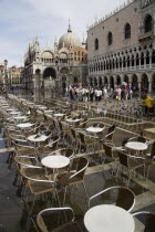 Aqua Alta High Water flooding in St Marks Square with restaurant tables in water by the Doges Palace with St Marks Basilica beyond