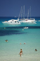 Pleasure boats at Cala Saona  Formentera  with a few people swimming in the sea.  TourismHolidaysBeachSunshine