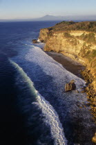 View north at sunset from Uluwatu Temple along rocky coastline towards distant volcano craters.