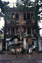 Decayed French colonial style residential buildings with people sheltering from the rain on the pavement