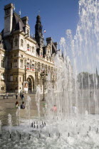 The Hotel de Ville town hall with people in the square in front of it seen through a water fountainFrench Western Europe European