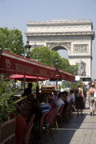 Tourists eating lunch at tables under shade in the Champs Elysees with the Arc de Triomphe in the distanceFrench Western Europe European