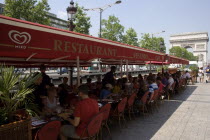 Tourists eating lunch at tables under shade in the Champs Elysees with the Arc de Triomphe in the distanceFrench Western Europe European