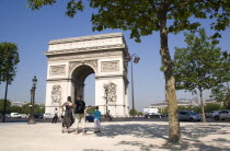 Tourist family standing in the shade of a tree in Place de Charles de Gaulle looking at the Arc de Triomphe with traffic passing around itFrench Western Europe European