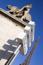 Street sign beside a stone statue on a pillar of a man standing beside a horse on the Pont dIena bridge with the Eiffel Tower beyondEquestrian European French Western Europe