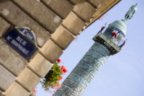 Street sign for Rue St Honore on a wall beside a window box with red geraniums and the statue of Napoleon in Place Vendome on the top of a column modelled on Trajans column in RomeEuropean French Rom...