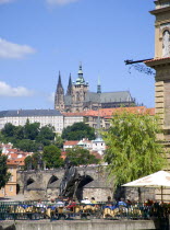 People sitting at tables outside the Smetana Museum on the banks of the Vltava River with the Charles Bridge and St Vituss Cathedral beyond in HradcanyPraha Ceska Eastern Europe European Religion