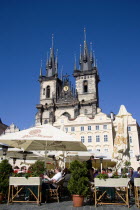 People seated at restaurant tables under umbrellas in the Old Town Square in front of the Church of Our Lady before TynPraha Ceska Eastern Europe European Religion