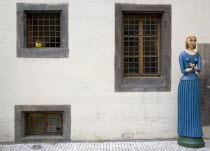 A carved and painted wooden figure of a woman holding a bird in both hands standing on the pavement outside the marionette museum in the Old TownPraha Ceska Eastern Europe European