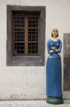 A carved and painted wooden figure of a woman holding a bird in both hands standing on the pavement outside the marionette museum in The Old TownPraha Ceska Eastern Europe European