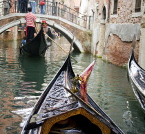 Gondolas carrying sightseeing tourists on a canal heading for a bridge in the San Marco district