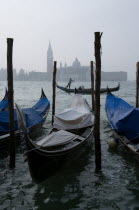 Gondolas moored by Molo San Marco with a gondola carrying tourists passing in the Basin with the Palladios church of San Giorgio Maggiore beyond on a misty day