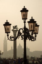 Tourist crowds in the Piazzatta beside the Doges Palace on a misty day with the Lion of St Mark on a column and San Giorgio Maggiore beyond