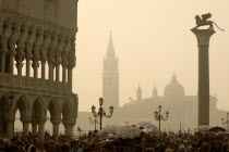 Tourist crowds in the Piazzatta beside the Doges Palace on a misty day with the Lion of St Mark on a column and San Giorgio Maggiore beyond