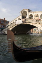 The bow or Ferro of a gondola moored on the Grand Canal beside the Rialto Bridge crowded with tourists