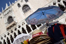 Souvenirs for sale at a stall in the Piazzetta below the 1536 balcony on the west facade of the Doges Palace with a carving of the Doge kneeling before the Lion of St Mark