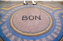 Pedestrian walk across a mosaic on the pavement with the word Bon at the centreCenter European French Western Europe