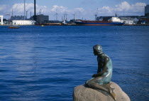 The Little Mermaid statue with port area and container ship behind.Danish Danmark European Northern Europe Scandinavia