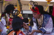 Chinese New Year.  Young woman applying make-up to another  both in costume with elaborate hair styles.Asian Prathet Thai Raja Anachakra Thai Religion Siam Southeast Asia Religious Siamese Asian Pra...