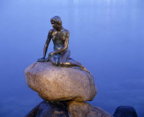 The Little Mermaid bronze statue seated on a rock at dusk with calm water Danish Danmark Northern Europe Scandinavia