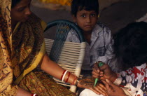 Woman having the palms of her hands decorated in Henna for her wedding with small boy onlookingAsia Bharat Inde Indian Intiya Kids Marriage Religion Religious Asian Religion Religious Hinduism Hindus...