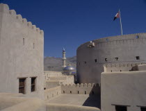 Minaret and blue and gold domed roof of mosque seen from fort walls with barren mountainside behind.Middle East Omani Religion Religious United Arab Emirates Al-Imarat Al-Arabiyyah Al-Muttahidah Arab...