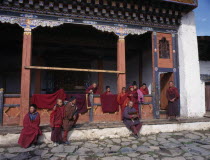 Group of young novice monks with older man holding cockerel gathered on step outside traditionally painted gompa or monastery.Asia Asian Bhutanese Druk Yul Male Men Guy Religion Religious Male Man Gu...