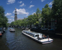 Pleasure boats on canal lined by trees and parked cars on side streets overlooked by typical architecture partly seen through branches.  Distant bridge and bell tower.North Automobiles Autos Benelux...