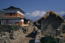 Woman walking between stone houses in Dharapani Village and the Dhaulagiri Himal snow capped mountain behind in the distanceAsia Asian Nepalese Female Women Girl Lady Scenic Female Woman Girl Lady On...