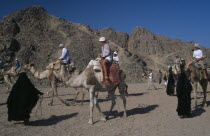 Bedouin women dressed in black leading tourists along on camelsAfrican Middle East North Africa Female Woman Girl Lady Female Women Girl Lady