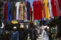 Sharia el-Souk street in the main market / bazaar. Men and women walking amongst market stalls under hanging displays of brightly coloured clothingAfrican Middle East North Africa Colored Female Woma...