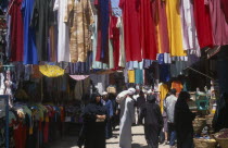 Sharia el-Souk street in the main market / bazaar. Men and women walking amongst market stalls under hanging displays of brightly coloured clothingAfrican Middle East North Africa Colored Female Woma...