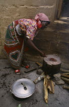 Woman refugee cooking beans in pot over open fire.