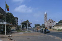 Street scene with church and passing cyclists and cars.