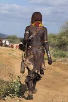 Hamer Jumping of the Bulls initiation ceremony  Hamer woman walking to the place where the bull jumping is being held. She wears a traditional goat skin dress decorated with cowrie shells  and her bac...