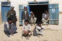 Group of men and young boys sat around a doorway.