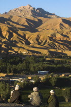 Men sit above Bamiyan village as the late afternoon sun glows on mountains near the empty niche where the famous carved Budda once stood  destroyed by the Taliban in 2001