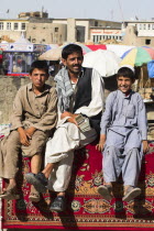 Money changer sits on rug on walls of Kabul river with street boys