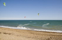 Kite Surfers on sea next to shingle beach in the summer with blue sky