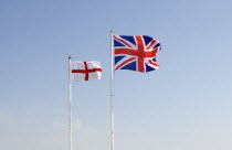 British Union Jack and St George Cross flags fyling against a blue sky