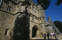 Battle Abbey. Angled view of The Gatehouse seen from under tree branches with visitors walking through