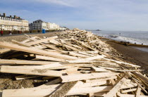 Timber washed up on the beach from the Greek registered Ice Princess which sank off the Dorset coast on 15th January 2008. People walk past on the promenade past seafront buildings with Worthing Pier...