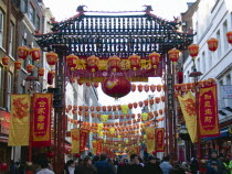 Crowds passing under paper lanterns hung around one of the oriental ornamental gates or paifang in Gerrard Street during Chinese New Year celebrations in 2006 for the coming Year of The Dog