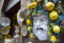 ITALY, Tuscany, San Gimignano, Outdoor shop display of ceramics with colourful plates and the face of a bearded man with fruit and vines in his hair.