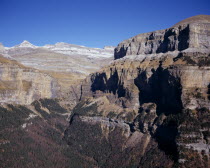 Circo de Cotatuero.  Sheer  eroded cliff showing grey  cream and brown coloured rock strata and steep  tree covered gully with cliffs of Muralla della Fraucata on right.