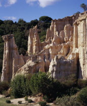 Ille Sur Tet.  Sandstone area known as Orgues.  Eroded sandstone cliff formed into pinnacles rising above shrubs and trees with tree covered hillside behind.