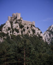 Chateau Puilarens.  Ruined medieval Cathar castle stronghold set high on limestone cliff showing keep.  With trees at foot of cliff in foreground.